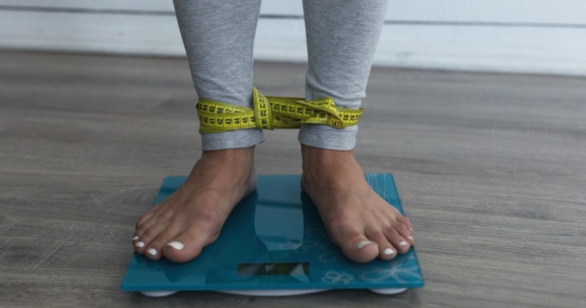 Mujer joven adulta vestida con indumentaria deportiva, subida a la balanza sin zapatillas para controlar su peso antes de calcular su imc