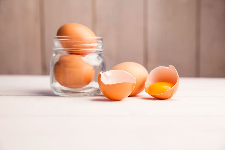 Huevos en un frasco y rotos que dejan ver la proteina y la grasa, macronutrientes esenciales para ganar masa muscular